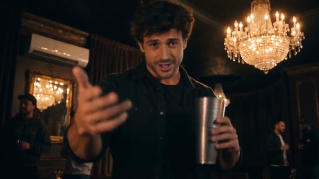 Lead performer faces the camera holding a metal cup in a chandelier-lit lounge